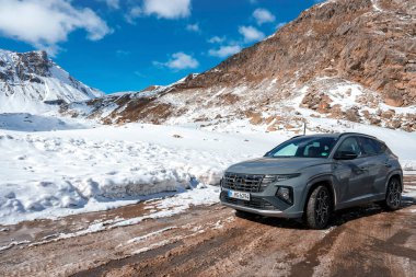 Yepyeni Hyndai Tucson 2023 SUV aracı yolun kenarına park edilmiş ve arka planda İsviçre 'de dağ aralığı ve berrak bir gökyüzü var..