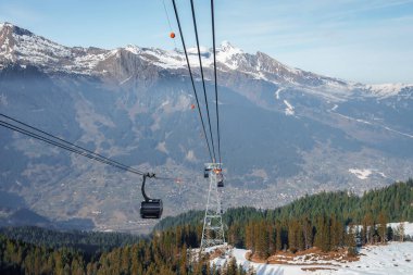 Gondol kaldıracı ormanda yetişen çam ağaçlarının üzerinde ilerliyor. Bernese dağlarının güzel manzarası ve arka planda gökyüzü var. İsviçre, Jungfrau 'da, kış tatili ve doğa konsepti.