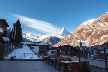 Saat kulesi ve şehirdeki binalar güzel karların önünde muhteşem dağlarla kaplı arka planda Zermatt, İsviçre, kış tatili konsepti.