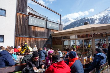 Sıcak giyimli erkek ve kadın turistler güneşli bir günde restoranda yemek yiyorlar, kış tatili konsepti.