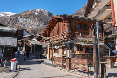 Zermatt, İsviçre 'de güneşli bir günde, arka planda dağ ve açık mavi gökyüzü ile eski kasabadaki ahşap dağ evi binaları arasındaki patika perspektifi giderek azalıyor.