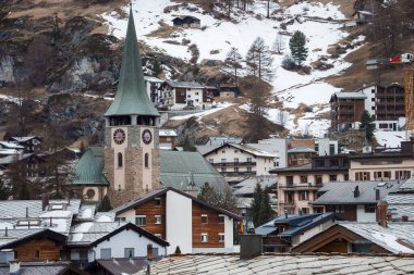 İsviçre 'nin Zermatt şehrinde etrafı karla kaplı yerleşim binalarıyla çevrili güzel saat kulesi manzarası, kış tatili konsepti.