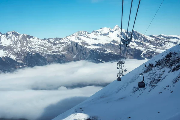 Gondola lifts moving on cables over snow covered hill with beautiful snowcapped Bernese mountains under sky at ski resort in Jungfrau, Switzerland, winter holiday and nature concept
