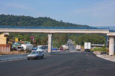 Asfalt üzerinde köprü ve açık mavi gökyüzü ile yeşil dağ güneşli bir günde, Kosta Rika kırsal yolunda arabalar ve kamyonlar