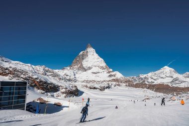 Zermatt, İsviçre 'de güneşli bir günde, kar üzerinde kayak yapan turistlerin manzarası ve dağ zirvesinin manzarası ve açık mavi gökyüzü, kış tatili konsepti.