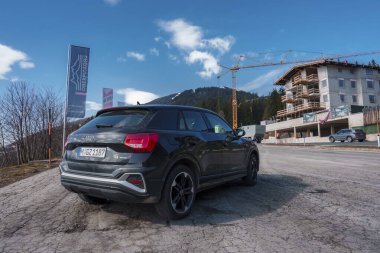 Gıcır gıcır Yeni Audi Q2 2023, yol kenarına park edilmiş, arka planda ve ormanda İsviçre dağları var..