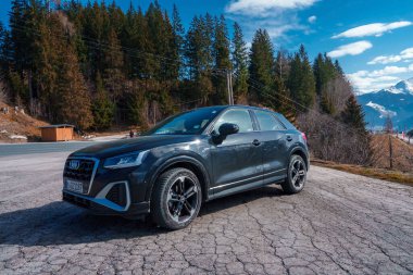 Gıcır gıcır Yeni Audi Q2 2023, yol kenarına park edilmiş, arka planda ve ormanda İsviçre dağları var..