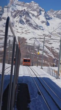 İsviçre 'nin Valais Alplerindeki Zermatt kayak merkezindeki ikonik çarklı Gornergrat trenine binmek güneşli bir kış gününde İsviçre' de trene binmek. Dikey video.