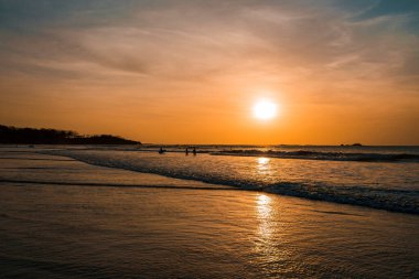Kosta Rika 'da gün batımında turuncu gökyüzünün altında yürüyen sörf tahtaları olan siluet arkadaşları, yaz tatili seyahat kavramı.