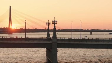 Riga, Letonya 'da yaz günbatımı. Gün batımında Letonya 'nın başkenti Riga' nın hava manzarası. Şehirden geçen güzel binalar, köprüler ve nakliye araçları.