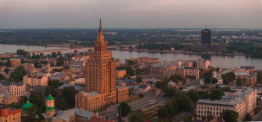 Riga, Letonya 'da yaz günbatımı. Gün batımında Letonya 'nın başkenti Riga' nın hava manzarası. Şehirden geçen güzel binalar, köprüler ve nakliye araçları.