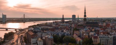 Riga, Letonya 'da yaz günbatımı. Gün batımında Letonya 'nın başkenti Riga' nın hava manzarası. Şehirden geçen güzel binalar, köprüler ve nakliye araçları.