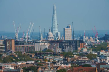 Arka planda mavi gökyüzü olan şehir manzarası. Londra 'daki yerleşim yerlerinin ortasındaki gökdelen ve katedral. Modern gelişimin yüksek açılı görünümü.