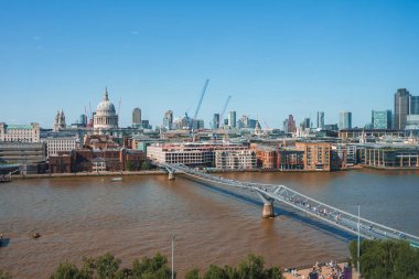 Thames Nehri üzerindeki Milenyum Köprüsü. Arka planda açık gökyüzü olan finans bölgesi. Londra 'da güneşli bir günde şehirdeki binalar.