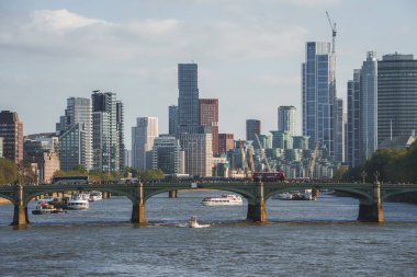 Westminster Köprüsü 'ndeki araçları uzaktan görebiliyoruz. Thames nehrinde modern binalarla hareket eden tekneler. Londra 'nın başkentinin manzaralı şehir güzelliği.