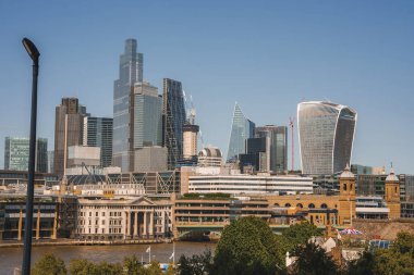 Arka planda açık mavi gökyüzü olan gökdelenler. Londra 'daki şehir merkezine Thames Nehri ile bakıyor. Güneşli bir günde finans bölgesi.