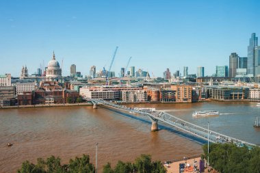 Güneşli bir günde Thames nehri üzerinde Milenyum Köprüsü. Arka planda açık gökyüzü olan finans bölgesi. Londra 'daki binalar.