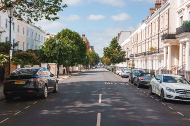 Notting Hill 'deki Pembridge Bahçeleri' nde lüks mülkler. Güneşli bir günde yola park edilmiş araçlar. Şehirdeki yaya yolunda yürüyen insanlar.