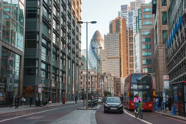 Erkek ve kadın turistler ofis binalarının önünden kaldırımda yürüyorlar. Araçlar finans bölgesinde yolda ilerliyor. Londra şehrindeki işlek cadde manzarası.