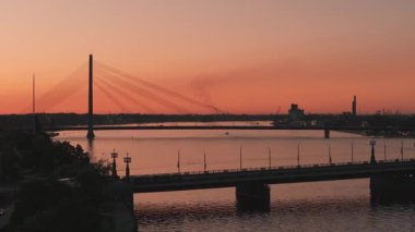 Riga şehrinin güzel hava manzarası - Letonya 'nın başkenti. Riga 'daki asma köprünün üzerinde günbatımı. Toplu taşımacılık köprüyü geçiyor.. 