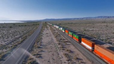 Taşıyıcı Tain hava görüntülerini taşıyor. Yük treni çöldeki demiryoluna çıkar. Lokomotif ve vagonlar. Çöl kumlu manzarası. Hava aracı görüntüsü.