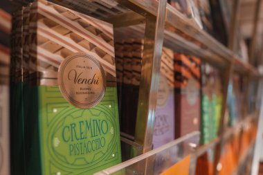 Bir dükkandaki cam bir kutuda çeşitli çikolataların düzenli bir şekilde sergilendiği bir kenar açı. Raflarda çeşitli aromalar ve kahverengi, turuncu ve beyaz çeşitleri sergileniyor..