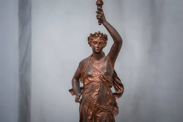 Bronze statue of woman holding torch on pedestal. Statue location and attire unknown. SEO: bronze sculpture, female figure, torch bearer, art, monument, historical, landmark.