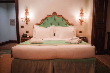 İtalya, Venedik 'teki Santa Maria Sarayı' nda lüks ve zarafet deneyimi. Bu resimde güzel dekore edilmiş beyaz ve yeşil yataklı bir oda, süslemeli lambalar ve gösterişli bir dekor var..