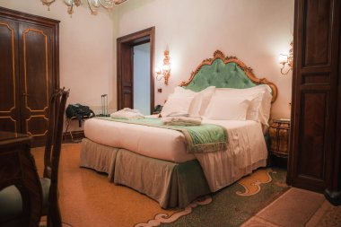 Venedik, İtalya 'da lüks bir otel odası. Büyük yatağı, beyaz yatağı, ahşap zemini ve çevresindeki avize ışıkları var. Beyaz, yeşil ve kahverengi renk düzeni zarif ve rahat bir atmosfer yaratır.