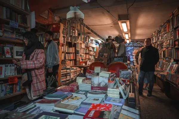 Çeşitli türde kitaplarla dolu samimi ve hareketli bir kitapçı keşfedin. Loş atmosfer ve kalabalık raflar kitap severler için davetkar ve sürükleyici bir deneyim yaratıyor..