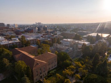 UCLA kampüsünün havadan görünüşü altın güneş ışığıyla yıkandı, Los Angeles 'ın geniş şehir manzarası ve uzak dağları arasında tarihi ve modern mimarinin bir karışımını sergiledi..