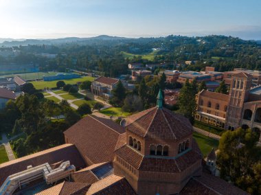 UCLA kampüsünün, Westwood, Los Angeles 'ta açık mavi gökyüzü altında Romanesk Uyanış mimarisini, yemyeşil ve kırmızı kiremitli çatılarını vurgulayan hava manzarası..