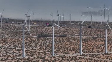 ABD 'nin Palm Springs kentindeki geniş ölçekli bir rüzgar türbini tarlasının havadan görünüşü, açık gökyüzünün altında altın-kahverengi çöl manzarası arasında durgun türbinler..