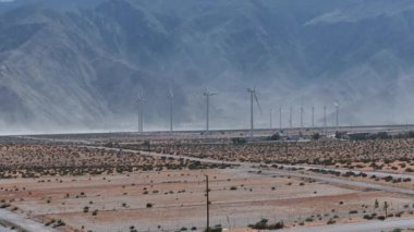 ABD 'nin Palm Springs kentindeki geniş ölçekli bir rüzgar türbini tarlasının havadan görünüşü, açık gökyüzünün altında altın-kahverengi çöl manzarası arasında durgun türbinler..