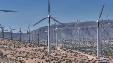 ABD 'nin Palm Springs kentindeki geniş ölçekli bir rüzgar türbini tarlasının havadan görünüşü, açık gökyüzünün altında altın-kahverengi çöl manzarası arasında durgun türbinler..