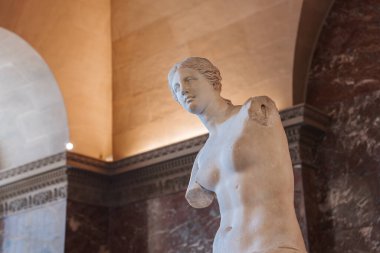 Beyaz mermer bir heykel, ifadesiz Venus de Milo örgülü saçlarıyla bir müzede sergileniyor..