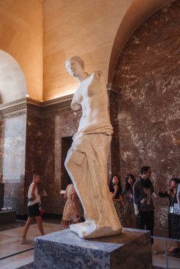 Gerçek boyutlarda, Venus de Milo adlı bir kadının heykeli. Sakin bir ifade, neoklasik kıyafetler ve müzede lüks saç stili..