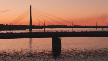 Riga şehrinin güzel hava manzarası - Letonya 'nın başkenti. Riga 'daki asma köprünün üzerinde günbatımı. Toplu taşımacılık köprüyü geçiyor.. 