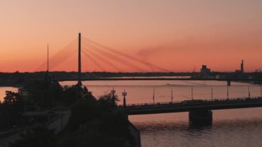 Riga şehrinin güzel hava manzarası - Letonya 'nın başkenti. Riga 'daki asma köprünün üzerinde günbatımı. Toplu taşımacılık köprüyü geçiyor.. 