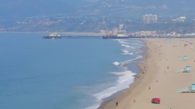 Los Angeles, ABD 'deki güzel Venedik plaj bölgesi. Venedik sahilinin havadan görünüşü, insanların sörf yapması, sahilde yürümesi ve farklı dükkanlara ve barlara girmesi..