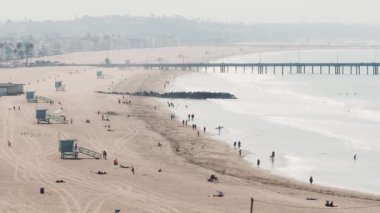 Los Angeles, ABD 'deki güzel Venedik plaj bölgesi. Venedik sahilinin havadan görünüşü, insanların sörf yapması, sahilde yürümesi ve farklı dükkanlara ve barlara girmesi..