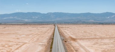 Amerika 'nın güneybatısının çorak manzarası boyunca uzanan sonsuz düz yolun klasik manzara manzarası. Yazın mavi gökyüzü ve güneşli güzel bir günde aşırı sıcak sis.