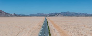 Amerika 'nın güneybatısının çorak manzarası boyunca uzanan sonsuz düz yolun klasik manzara manzarası. Yazın mavi gökyüzü ve güneşli güzel bir günde aşırı sıcak sis.