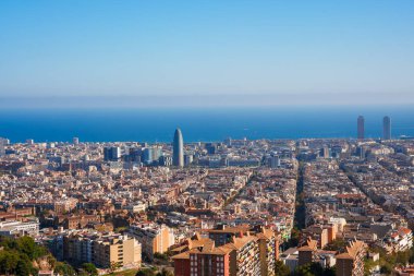 Berrak gökyüzü altındaki Barcelonas Eixample bölgesinin panoramik manzarası, kent şebekesini, Torre Glories 'i ve Olimpiyat Limanı yakınlarındaki kıyı siluetini gözler önüne seriyor.