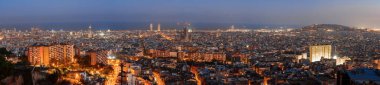 Barcelona, İspanya 'nın panoramik akşam manzarası, aydınlık caddeler ve binalarla aydınlık gökyüzüne karşı kentsel parlaklığını gösteriyor, kıyı manzarasını ve canlı gece hayatını ima ediyor..