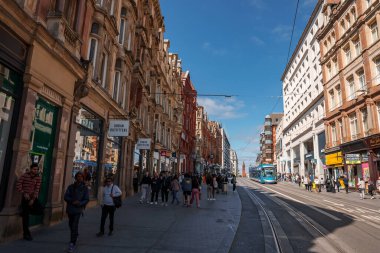 Birmingham, Birmingham 'da tarihi ve modern binalar, yayalar ve açık gökyüzü altında mavi bir tramvay, şehirlerin mimari çeşitliliğini ve kentsel yaşamı vurguluyor..