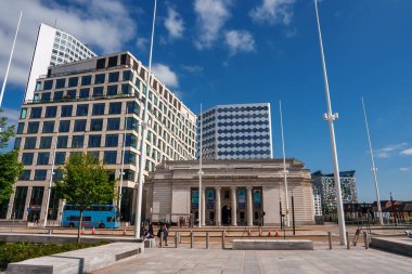 Birmingham, İngiltere 'de geniş bir plaza, açık mavi gökyüzü altındaki modern yapılarla çelişen, tarihin ve ilerlemenin şehir harmanını vurgulayan, sütunları olan klasik bir binaya çıkıyor..