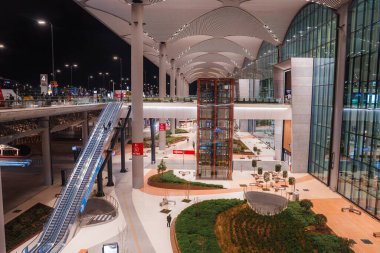 İstanbul Havaalanlarına bakan iç kısımda beyaz dalga kemerleri, yumuşak ışıklar, cam cephe, yürüyen merdiven, metro tabelaları, cam kaldırma, koltuklar ve santraller var..
