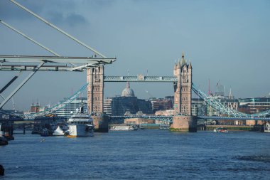 Gotik mimarisi ve Thames Nehri ile Londons Tower Bridge 'in sakin gündüz görüntüsü. St. Pauls Katedrali, açık mavi gökyüzünün ortasındaki arka planı şereflendirir..