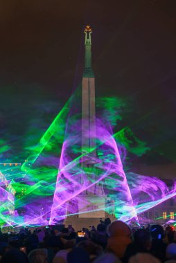 Riga 'daki aydınlık yeşil ve mor ışıklarla süslenmiş Özgürlük Anıtı' nın önünde Letonya 'nın Bağımsızlık Günü' nde akşam kutlamaları var..